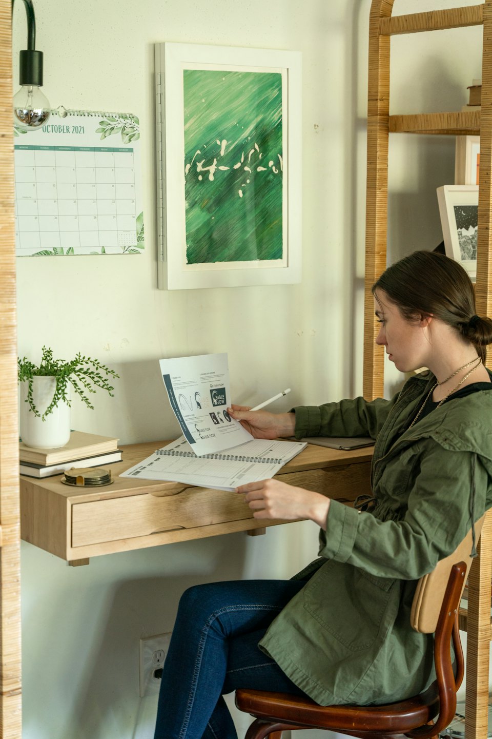 Woman reviews document at desk with stylus in home office.