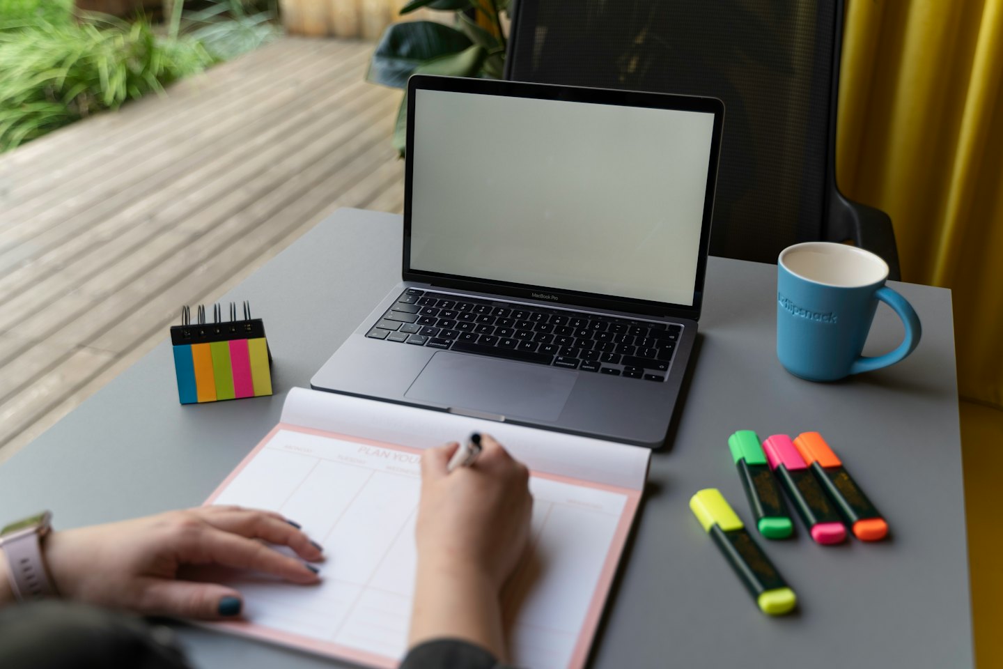 Hands writing in a planner next to an open laptop.